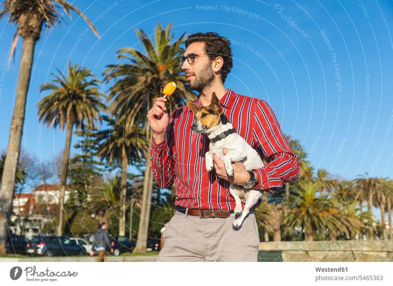Junger Mann mit Hund auf dem Arm isst Eis Lolly Single Alleinstehende Unverheirateter Singles Alleinstehender Palme Palmen ein Tier 1 Einzelnes Tier einzeln