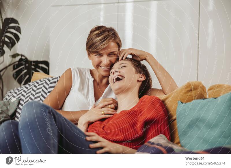 Glückliches lesbisches Paar lachend und kuschelnd auf Couch glücklich glücklich sein glücklichsein Pärchen Paare Partnerschaft schmusen knuddeln Sofa Couches