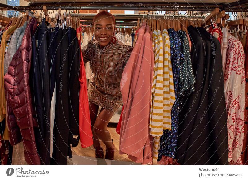 Junge Frau mit farbenfrohem Haarschnitt zwischen den Kleidern in einem Geschäft Kauf Einkauf Einkaufen shoppen shopping freuen Glück glücklich sein