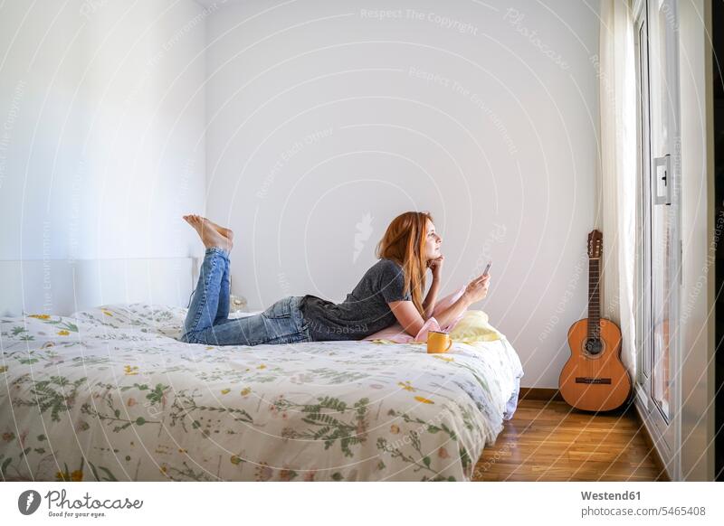 Junge Frau zu Hause chillt im Schlafzimmer und benutzt ihr Smartphone Leute Menschen People Person Personen Europäisch Kaukasier kaukasisch 1 Ein ein Mensch