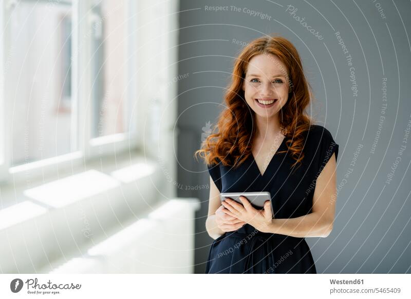 Porträt einer zufriedenen rothaarigen Geschäftsfrau mit digitalem Tablet in einem Loft Leute Menschen People Person Personen Europäisch Kaukasier kaukasisch 1