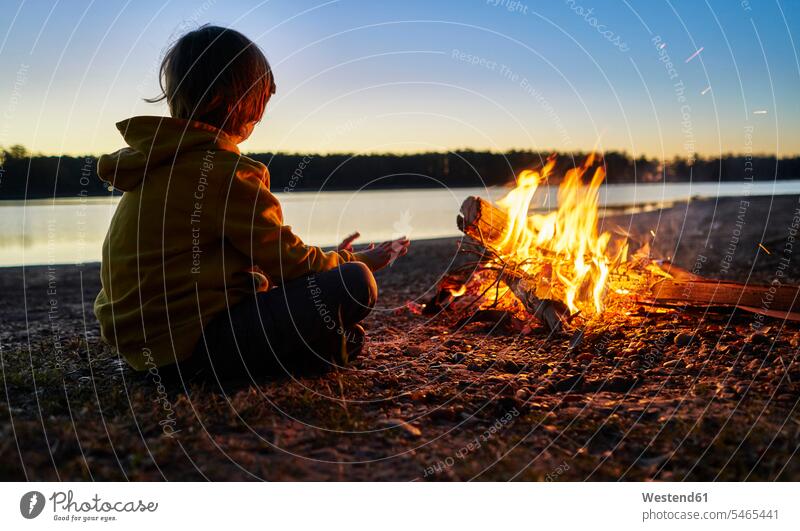 Argentinien, Patagonien, Concordia, Junge sitzt am Lagerfeuer an einem See Buben Knabe Jungen Knaben männlich Seen sitzen sitzend Kind Kinder Kids Mensch