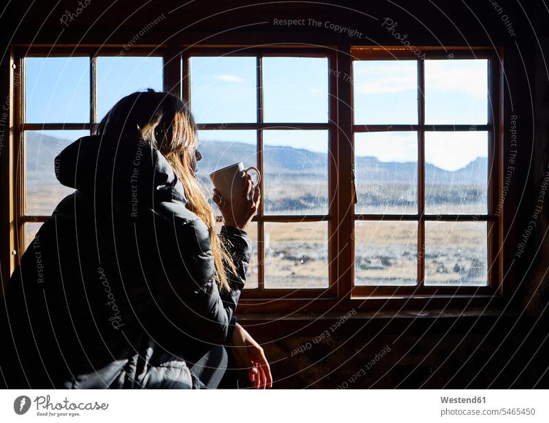 Frau trinkt eine Tasse Kaffee, während sie durch das Fenster die Berge bewundert Touristen Fensterscheiben Glasscheiben entspannen relaxen sitzend sitzt