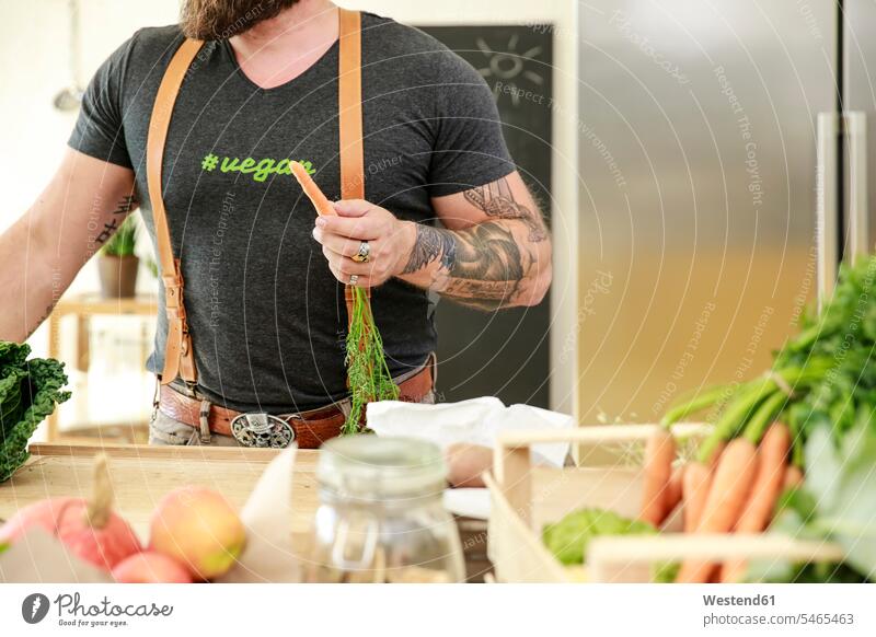 Veganer Mann hält Karotte in seiner Küche reifer Mann reife Männer Karotten Mohrrüben Möhre Möhren Gemüse Gemuese vegan vegane kochen Vegetarier Vegetarismus