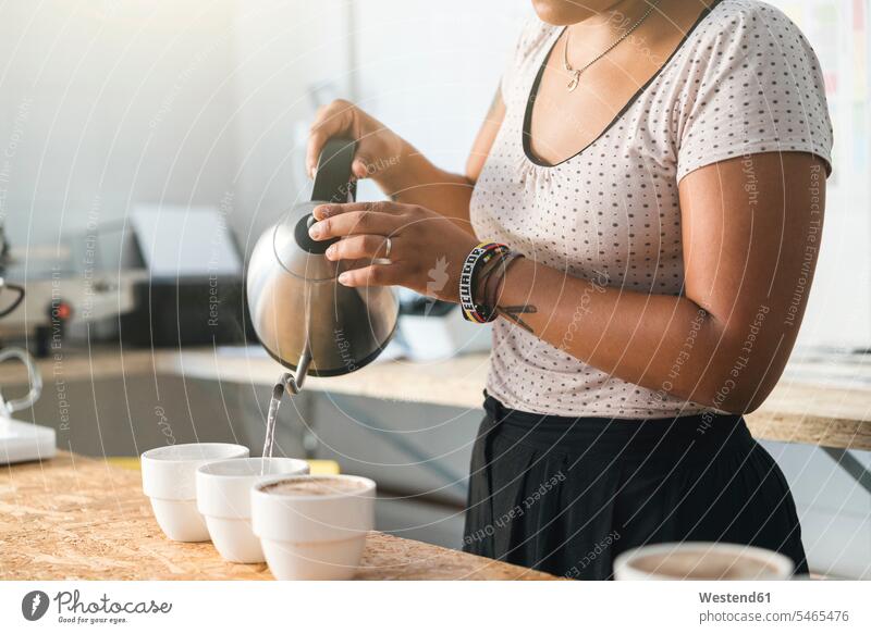 Nahaufnahme einer Frau, die in einer Kaffeerösterei arbeitet und heißes Wasser in Kaffeetassen gießt Leute Menschen People Person Personen gemischtrassig 1 Ein