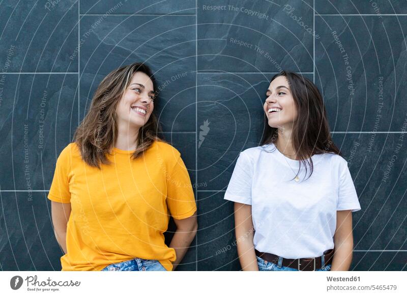 Zwei Freunde, die sich an eine graue Wand lehnen und lachen Leute Menschen People Person Personen Europäisch Kaukasier kaukasisch Südeuropäisch 2 2 Menschen