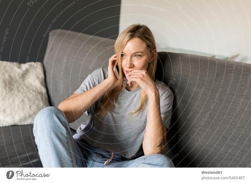 Lächelnde junge Frau sitzt auf der Couch und spricht mit dem Handy weiblich Frauen lächeln telefonieren anrufen Anruf telephonieren sitzen sitzend Mobiltelefon