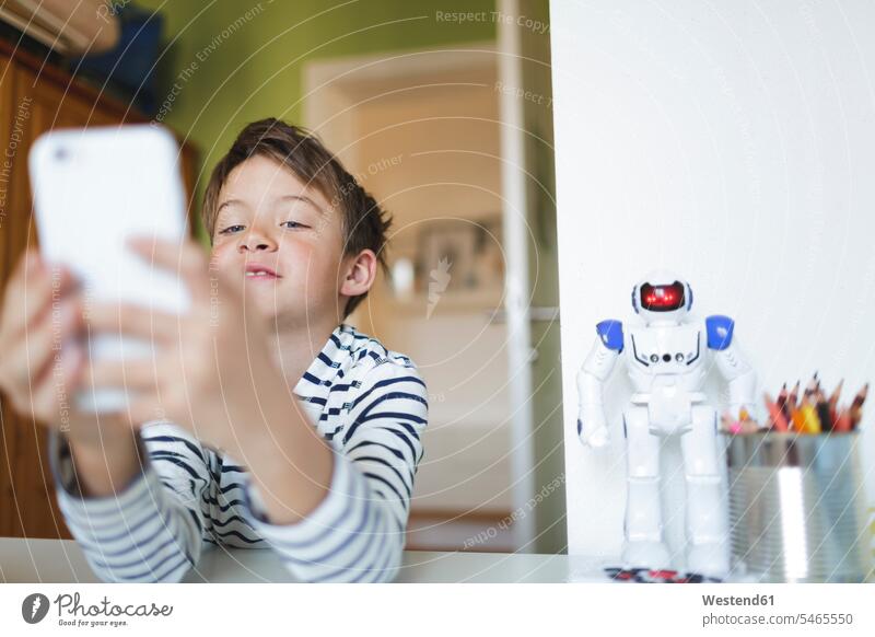 Junge, der zu Hause unterrichtet und zu Hause ein Smartphone benutzt Schreibtisch Roboter Handy lernen spielen Zuhause Freizeit Online Allein Digital
