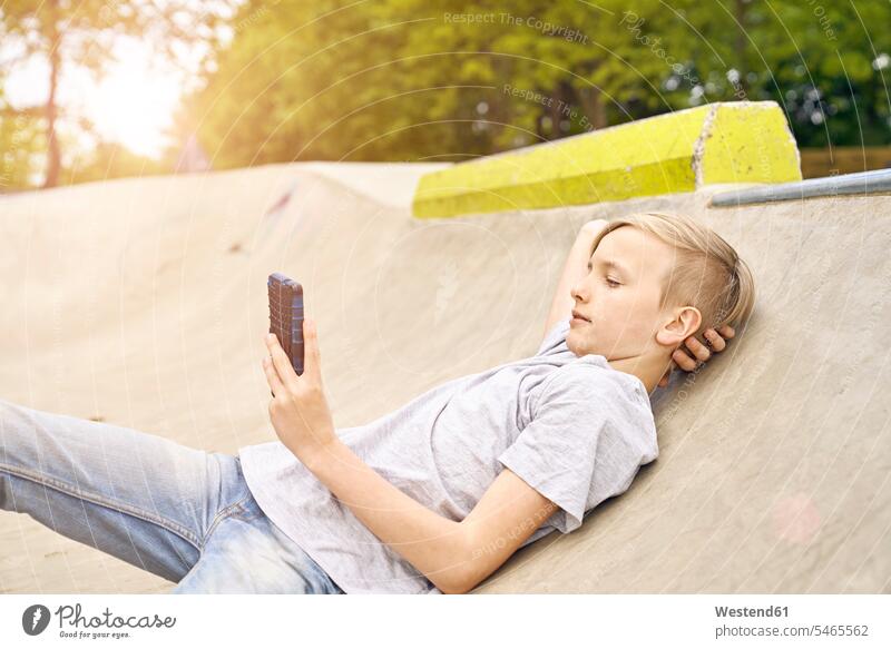 Junge benutzt Smartphone im Skatepark Freizeit Muße betrachten betrachtend ansehen liegen liegend liegt Buben Knabe Jungen Knaben männlich iPhone Smartphones