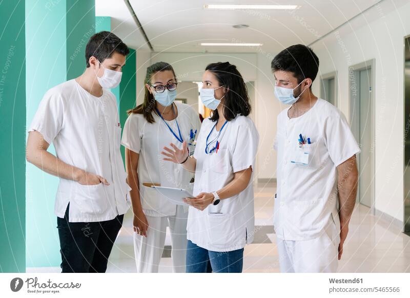 Ärzte mit Operationsmasken diskutieren im Krankenhaus stehend über ein digitales Tablett Farbaufnahme Farbe Farbfoto Farbphoto Spanien Innenaufnahme