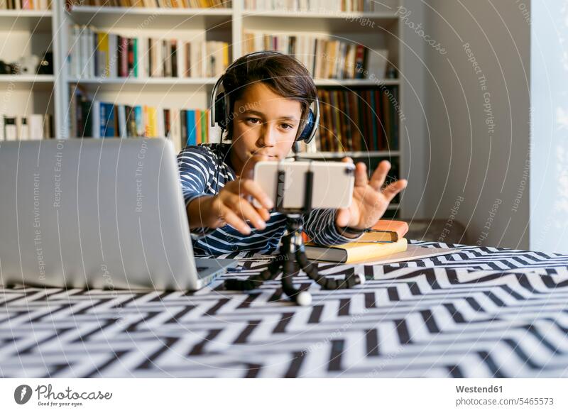 Junge, der sein Smartphone auf einem Stativ einstellt und neben seinem Laptop am Tisch sitzt Farbaufnahme Farbe Farbfoto Farbphoto 8-9 Jahre 8 bis 9 Jahre