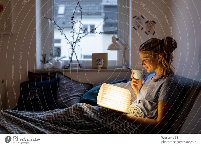 Junge Frau liest zu Hause auf dem Sofa ein illuminiertes Buch Leute Menschen People Person Personen Europäisch Kaukasier kaukasisch 1 Ein ein Mensch eine
