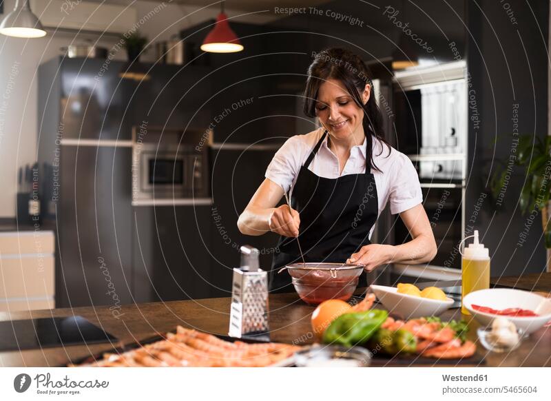 Lächelnde Frau, die in der Küche kocht und eine Soße abseiht Spanien grüne Paprika Küchensieb Sieb Kuechensiebe Küchensiebe Wohnung wohnen Wohnungen Zutaten
