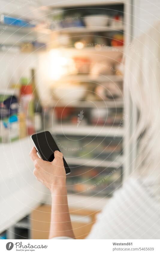 Hand einer Frau mit Smartphone, die den Kühlschrank in der Küche im Smart Home überprüft Küchen weiblich Frauen überprüfen testen checken Hände Zuhause zu Hause