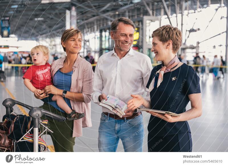 Glückliche Familie zeigt dem Mitarbeiter der Fluggesellschaft am Flughafen die Pässe Angestellte Mitarbeiterin Gepäckwagen Flughaefen Flugplätze Airport