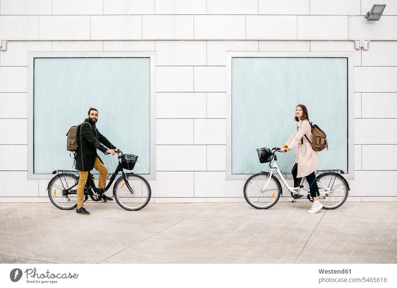 Porträt von Mann und Frau mit E-Bikes an einem Gebäude stehend Portrait Porträts Portraits eBikes Elektrofahrrad Elektrorad Stadt staedtisch städtisch Paar