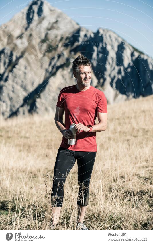 Österreich, Tirol, lächelnde Sportlerin auf Almwiese stehend Bergwiese Bergwiesen Gebirge Berglandschaft Gebirgslandschaft Gebirgskette Gebirgszug Berge steht