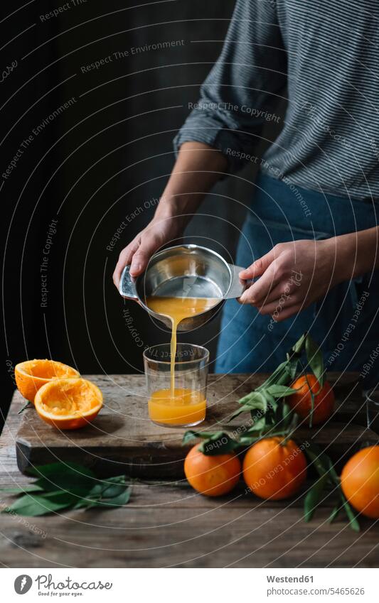 Junger Mann gießt frisch gepressten Orangensaft in ein Glas, Teilansicht jung Apfelsinensaft O-Saft Männer männlich ausgepresst schütten einschenken gießen