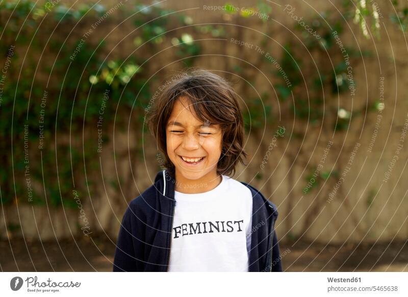 Lachender Junge steht auf der Straße mit Aufdruck auf T-Shirt und sagt Feministisch T-Shirts freuen Frohsinn Fröhlichkeit Heiterkeit witzig humorvoll lustig