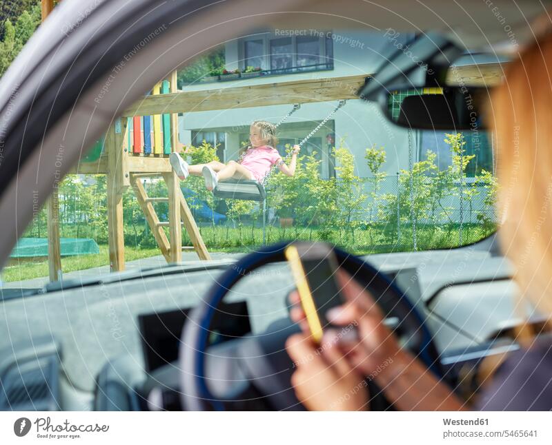 Mädchen auf Schaukel und Frau im Elektroauto simsen mit dem Handy Schaukeln weiblich Frauen Auto Wagen PKWs Automobil Autos Mobiltelefon Handies Handys