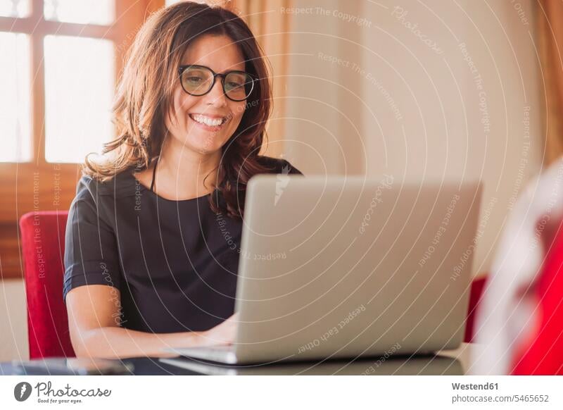 Glückliche Geschäftsfrau, die zu Hause arbeitet, während sie im Wohnzimmer einen Laptop benutzt Farbaufnahme Farbe Farbfoto Farbphoto Spanien Innenaufnahme