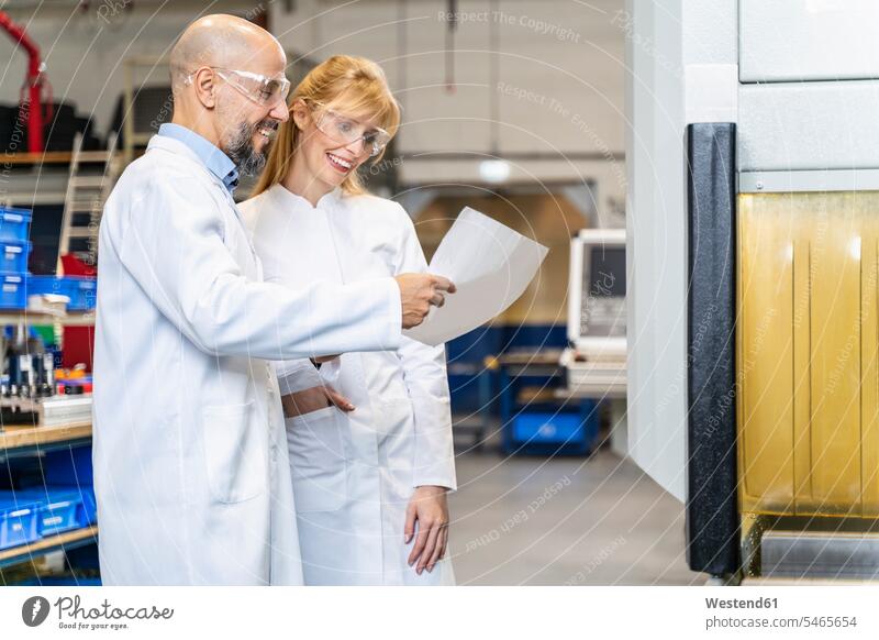Zwei glückliche Techniker in Laborkitteln und mit Schutzbrille betrachten einen Plan in einer Fabrik Pläne Fabriken Schutzbrillen Brille Glück glücklich sein
