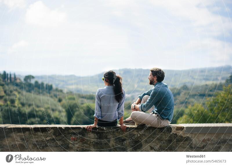 Ein Paar betrachtet die Landschaft, während es auf einer Stützmauer gegen den Himmel sitzt Farbaufnahme Farbe Farbfoto Farbphoto Toskana Italien Tourismus