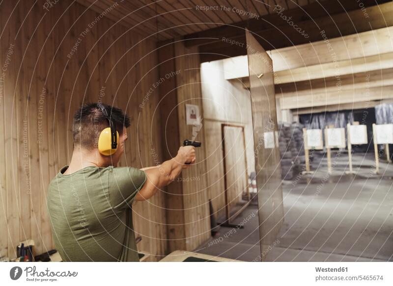 Mann zielt mit einer Pistole in einer Indoor-Schießanlage Pistolen Schußwaffe Männer männlich schießen zielen zielend Schießstand Schiessstaende Schießstände