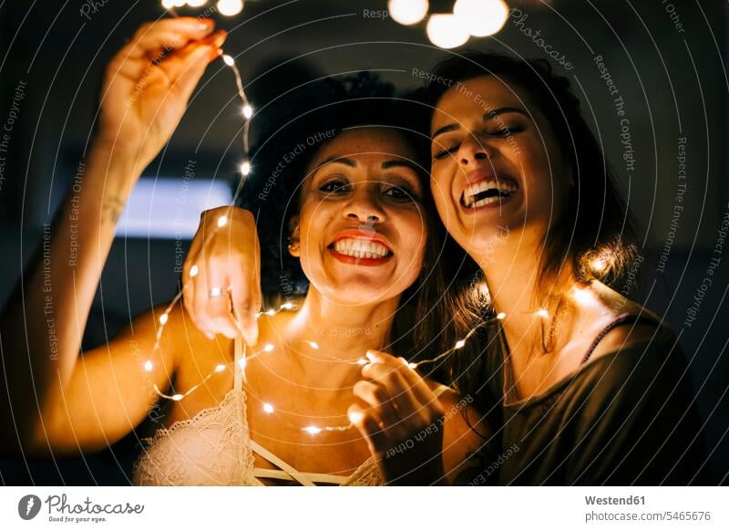 Nahaufnahme von fröhlichen Freundinnen, die zu Hause Lichterketten in der Hand halten Farbaufnahme Farbe Farbfoto Farbphoto Portugal Freizeitbeschäftigung Muße