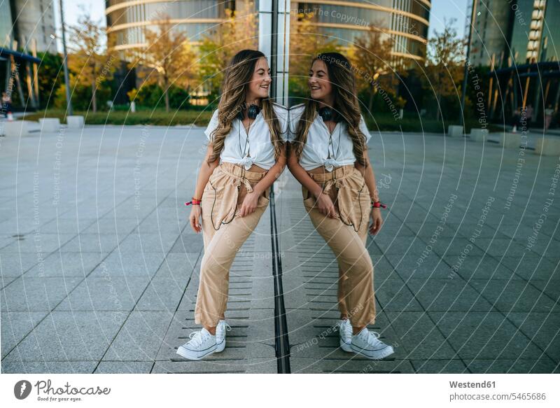 Junge lächelnde Frau, die sich in Glas spiegelt und sich selbst betrachtet Leute Menschen People Person Personen Europäisch Kaukasier kaukasisch 1 Ein