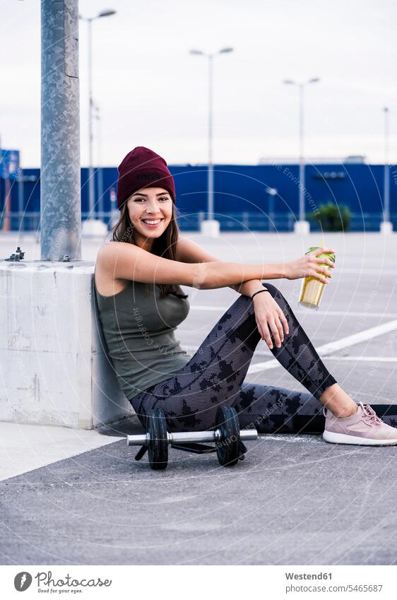 Junge Frau sitzt nach Hanteltraining auf dem Boden und trinkt Saft aktiv trinken sitzen sitzend Pause Pause machen Fitness fit Gesundheit gesund Kraft stark