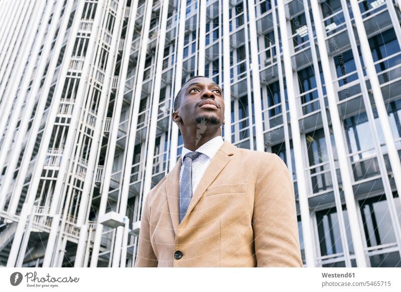 Junger Geschäftsmann vor modernem Bürogebäude in der Stadt mit seitlichem Blick geschäftlich Geschäftsleben Geschäftswelt Geschäftsperson Geschäftspersonen