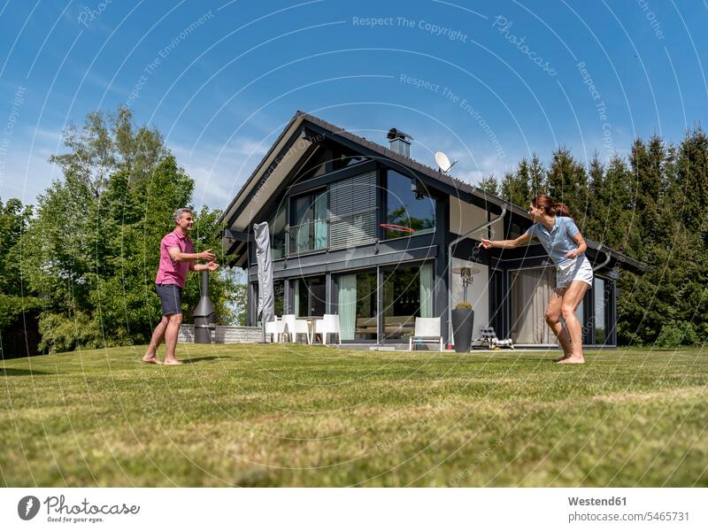 Glückliches Paar spielt mit fliegender Scheibe im Garten seines Hauses Wurfscheibe Frisbee Wurfscheiben Flugscheiben Pärchen Paare Partnerschaft Gärten Gaerten