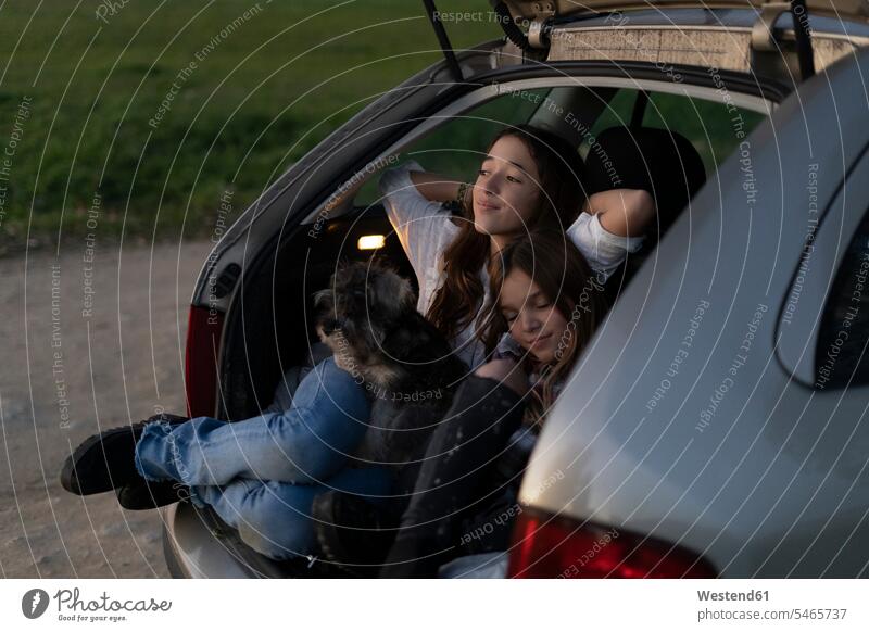 Zwei Schwestern im geöffneten Kofferraum eines geparkten Autos beobachten den Sonnenuntergang offen aufgeklappt Sonnenuntergänge Wagen PKWs Automobil Gepäckraum