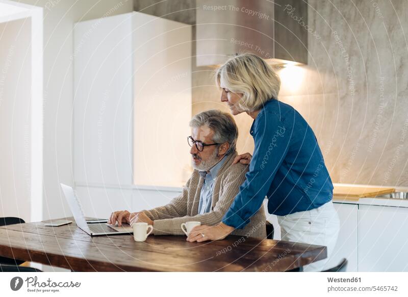 Reifer Mann mit Frau, der zu Hause einen Laptop auf dem Küchentisch benutzt Leute Menschen People Person Personen Europäisch Kaukasier kaukasisch 2 2 Menschen