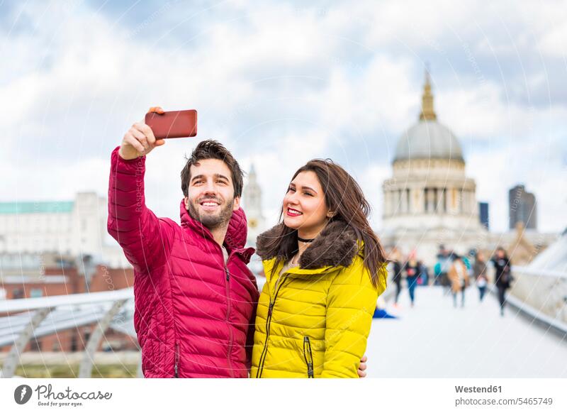 UK, London, Porträt eines lächelnden jungen Paares, das ein Selfie mit seinem Handy vor der St. Pauls Cathedral macht Smartphone iPhone Smartphones Portrait