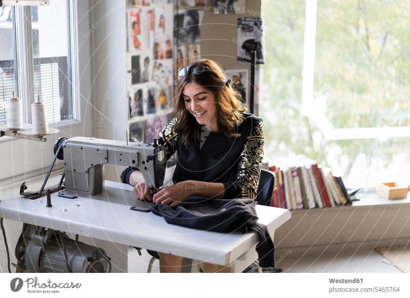 Lächelnde junge Modedesignerin mit Nähmaschine in ihrem Atelier lächeln benutzen benützen Nähmaschinen Naehmaschinen Modedesignerinnen Elektrogerät