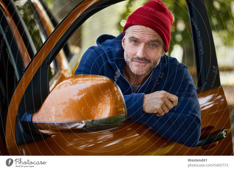 Porträt eines bärtigen reifen Mannes mit roter Mütze, der sich aus dem Fenster einer offenen Autotür lehnt Türen Wagentüren Tueren Wagentueren Autotuer