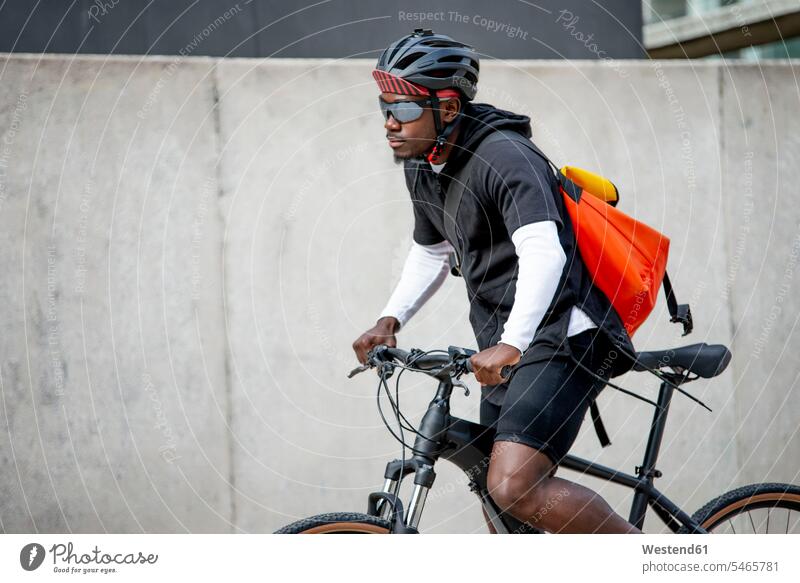 Stilvoller junger Mann mit Kuriertasche beim Fahrradfahren in der Stadt Leute Menschen People Person Personen Afrikanisch Afrikanische Abstammung dunkelhäutig