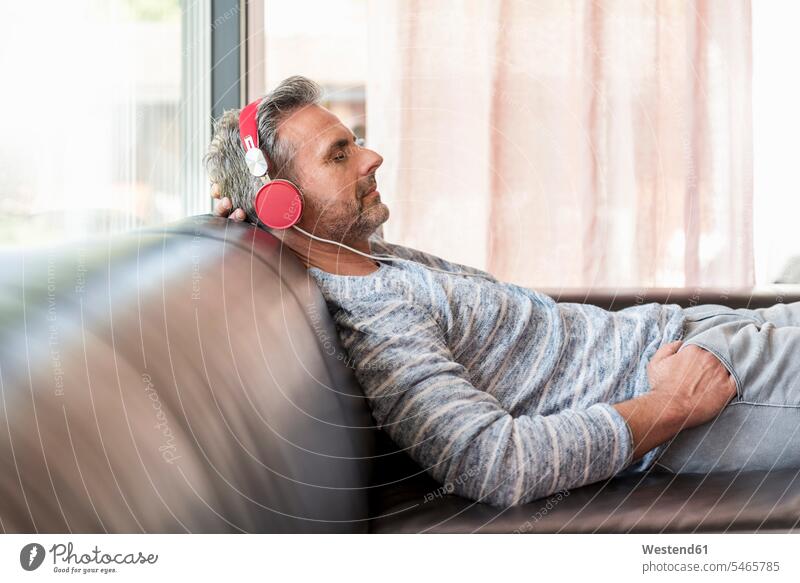 Entspannter reifer Mann, der zu Hause auf der Couch liegt und Kopfhörer trägt Zuhause daheim liegen liegend entspannt entspanntheit relaxt Kopfhoerer Sofa