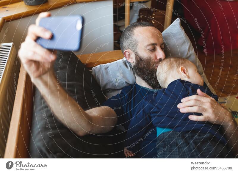 Mann macht ein Selfie mit seinem süßen schlafenden Sohn auf dem Sofa Polster Couch Couches Liege Sofas Telekommunikation telefonieren Handies Handys
