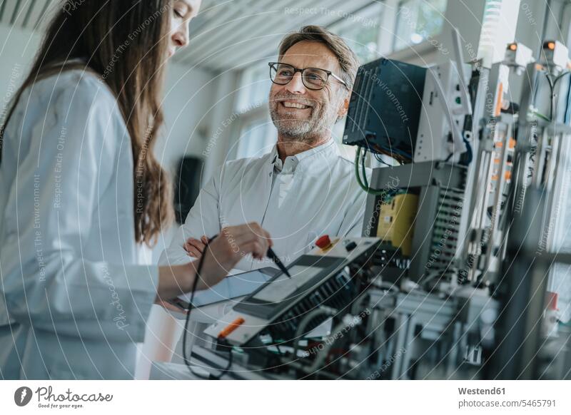 Lächelnder Mann schaut eine Kollegin an, die im Labor Maschinen bedient Farbaufnahme Farbe Farbfoto Farbphoto Innenaufnahme Innenaufnahmen innen drinnen