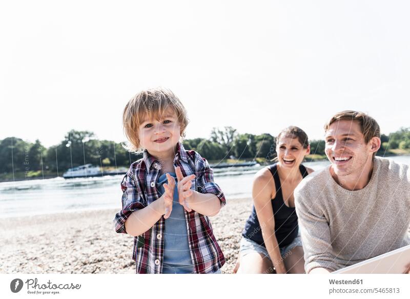 Glücklicher Junge klatscht Hände am Flussufer mit beobachtenden Eltern glücklich glücklich sein glücklichsein fröhlich Fröhlichkeit Frohsinn Heiterkeit Sohn