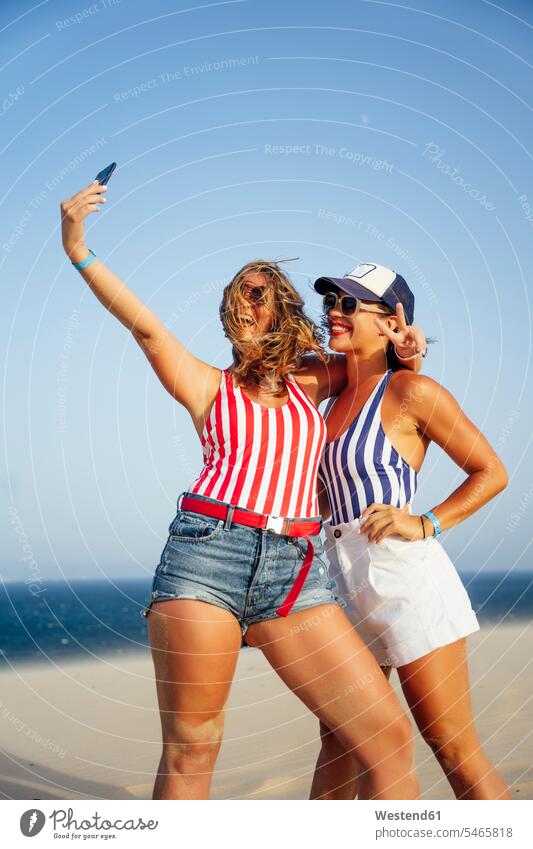 Fröhliche Freundinnen, die am Strand vor klarem Himmel stehen und sich mit sich selbst beschäftigen Farbaufnahme Farbe Farbfoto Farbphoto Spanien Außenaufnahme