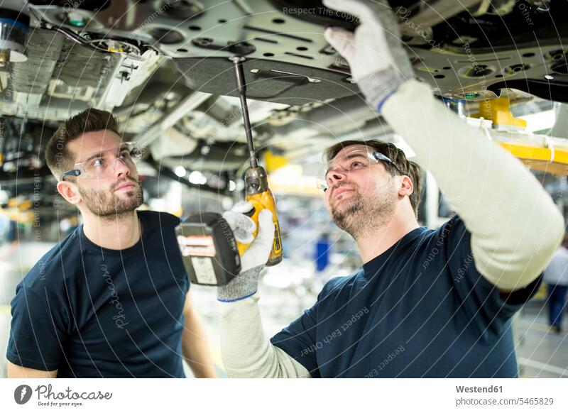 Zwei Kollegen arbeiten am Autounterboden in einer modernen Fabrik Arbeitskollege Arbeitskollegen Job Berufe Berufstätigkeit Beschäftigung Jobs Arbeiter T-Shirts