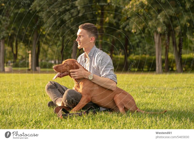 junger Mann mit seinem Hund, kuschelnd auf einer Wiese Tiere Tierwelt Haustiere Hunde sitzend sitzt freuen Glück glücklich sein glücklichsein innig nah