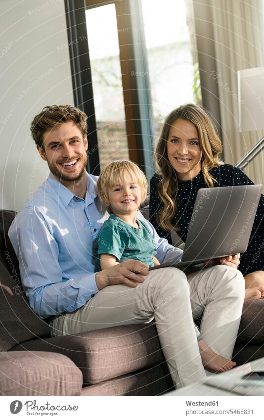 Porträt von glücklichen Eltern und ihrem Sohn, die zu Hause auf einem Sofa mit Laptop sitzen Glück glücklich sein glücklichsein Couches Liege Sofas lächeln