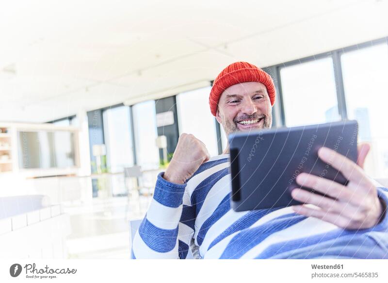 Glücklicher Mann jubelt, während er zu Hause ein digitales Tablet benutzt Farbaufnahme Farbe Farbfoto Farbphoto Innenaufnahme Innenaufnahmen innen drinnen Tag