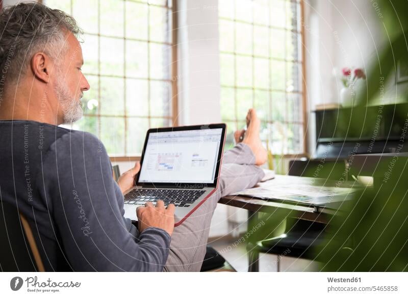 Reifer Mann, der vom Heimbüro aus mit den Füßen nach oben und mit einem Laptop arbeitet sitzen sitzend sitzt Laptop benutzen Laptop benützen Füße hochlegen