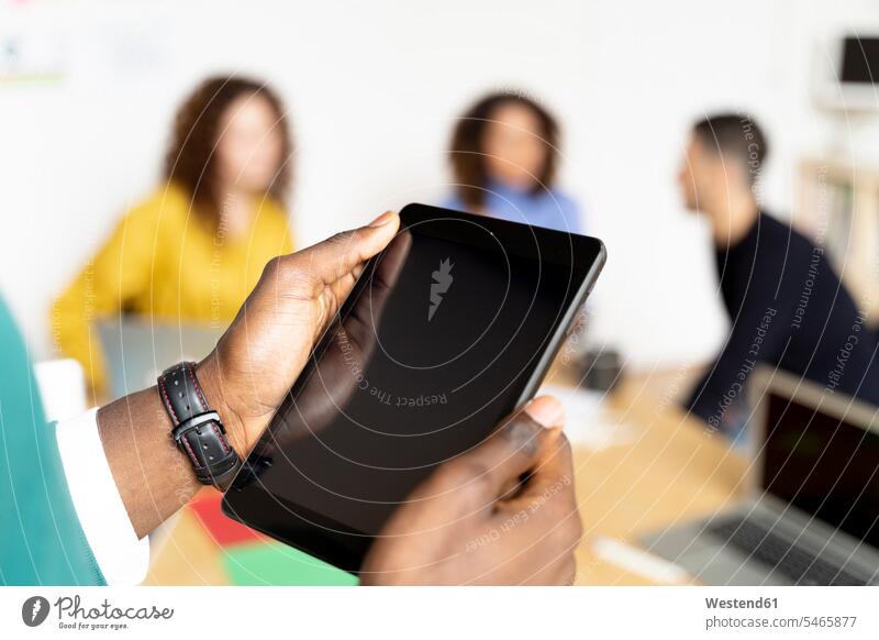 Nahaufnahme eines Geschäftsmannes im Büro mittels Tablett mit Kollegen im Hintergrund Leute Menschen People Person Personen gemischtrassig Afrikanisch